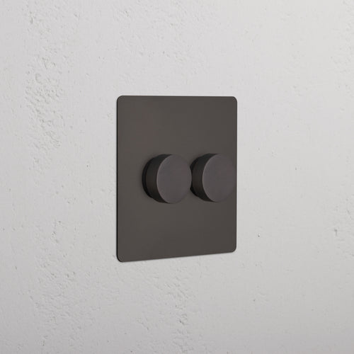 Bronze Kew 2G Dimmer Switch featuring two round knobs, installed on a white wall.
