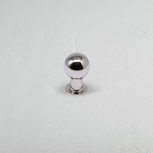 Small polished nickel Bayswater furniture knob with spherical head and short base on a light gray surface.