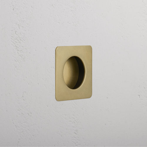 Regent Recessed Small Pull in antique brass, square shape with circular indent, mounted on white wall.