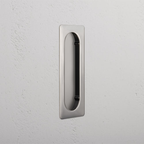 Regent Recessed Medium Pull in Polished Nickel, a rectangular cabinet handle with rounded edges, mounted on a wall.