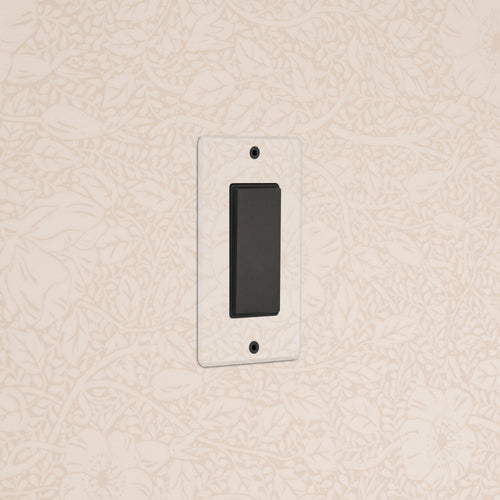 Kew 1G Center Retractive Rocker Switch in Clear Bronze Black, mounted on a floral-patterned beige wall.