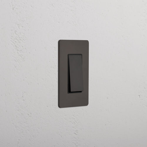 Grove 1G Retractive Rocker Switch in Bronze Black, single rectangular switch on a white textured wall.