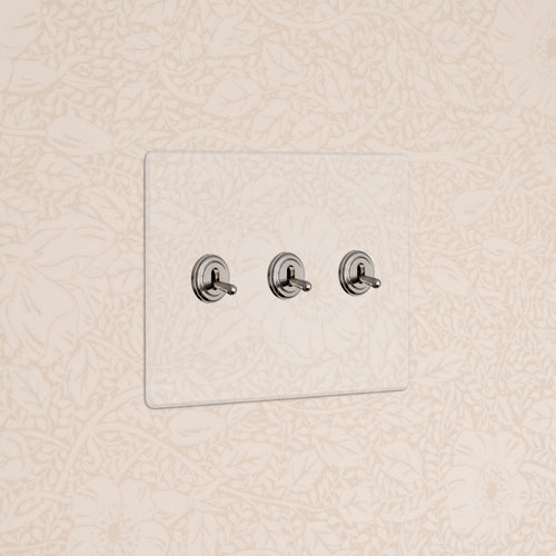 Kew 3G Toggle Switch in Clear Polished Nickel with three toggles, shown on a beige floral-patterned wall.