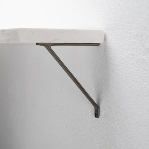 Close-up of a Brixton Shelf Bracket Small in bronze, mounted on a textured white wall supporting a shelf.