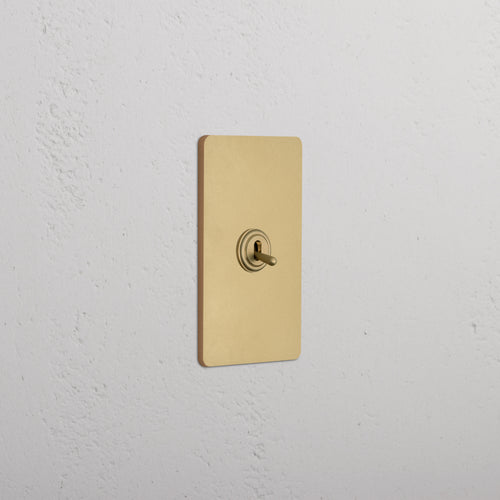 Grove 1G Retractive Toggle Switch in antique brass finish, shown installed on a white wall.