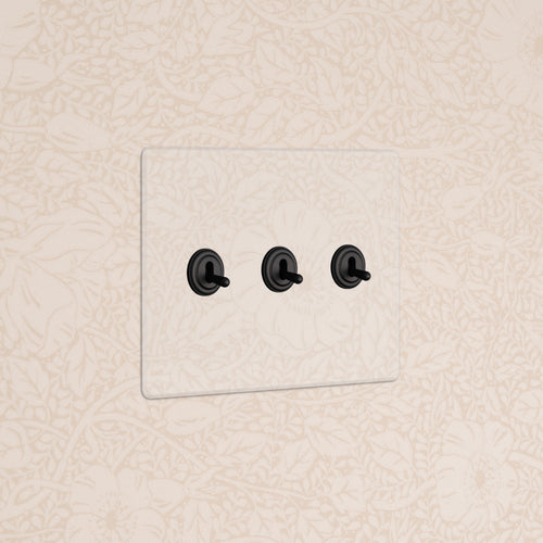 Kew 3G Toggle Switch in Clear Bronze finish with three black toggles, mounted on a beige patterned wall.