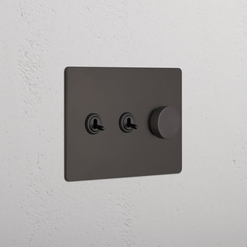 Grove 3G 2x Toggle & Dimmer Switch in bronze with two toggles and a round dimmer knob on a wall.