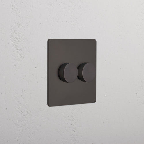 Bronze Grove 2G Dimmer Switch with two round knobs, mounted on a textured white wall.