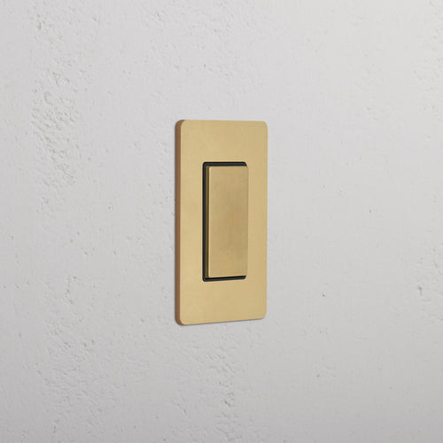 Grove 1G Center Retractive Rocker Switch in Antique Brass Black with rectangular plate on white wall.