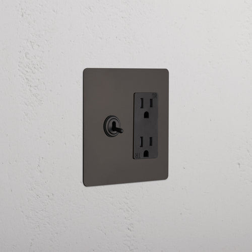 Kew 2G Toggle Switch & Outlet in Bronze Black with two toggles and a single outlet on a dark rectangular plate.