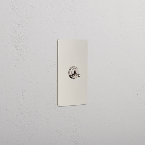 Kew 1G Dimming Retractive Toggle Switch in Polished Nickel, mounted on a white textured wall.