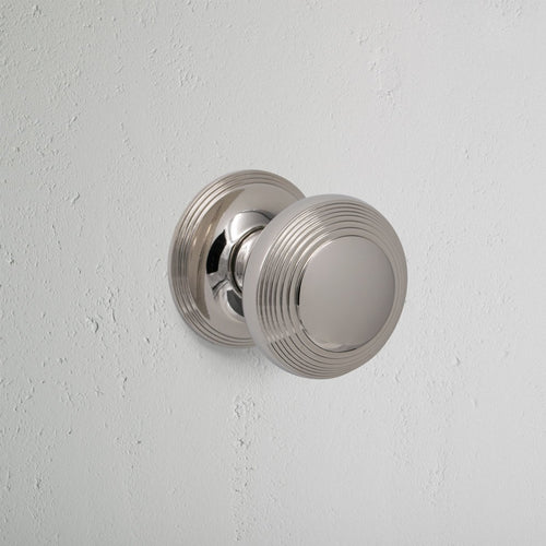 Polished nickel Poplar Dummy Door Knob Set with round, ridged design mounted on a white wall.