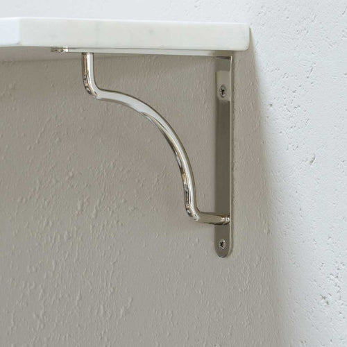 Kilburn Shelf Bracket Small in polished nickel, mounted on a wall and supporting a white shelf.