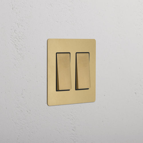 Kew 2G Rocker Switch in antique brass with black inserts, mounted on a white textured wall.