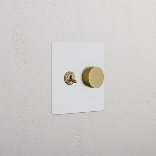 Kew 2G Toggle & Dimmer Switch in paintable antique brass finish, shown on a textured white wall.