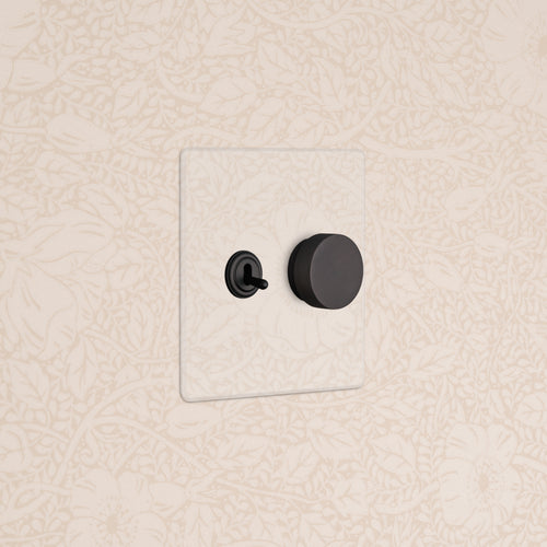 Kew 2G Toggle & Dimmer Switch in clear bronze with black toggle and round dimmer on a beige floral wall.