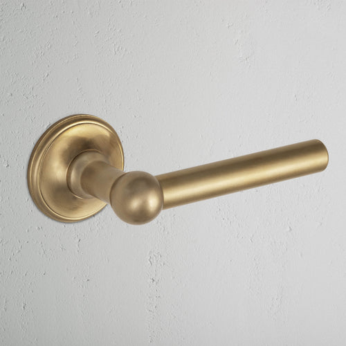 Harper Passage Door Handle Set in antique brass with a round baseplate, mounted on a white wall.