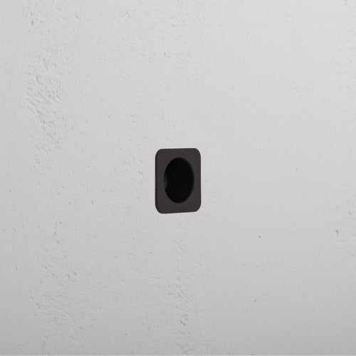 Regent Recessed Edge Pull in bronze, square design, installed flush in a white textured wall.