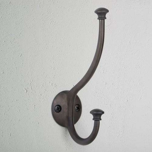 Bronze Mews Hook wall-mounted coat hook with two prongs, attached to a white textured wall.