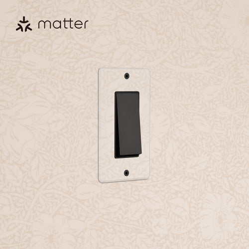 Kew 1G Smart Retractive Rocker Switch in Clear Bronze Black with clear wall plate on a beige patterned wall.