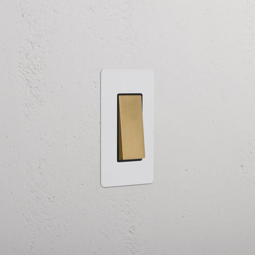 Kew 1G Rocker Switch in paintable antique brass with black switch, shown against a white wall.