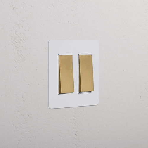 Kew 2G Rocker Switch in paintable antique brass white finish on a rectangular plate against a white wall.