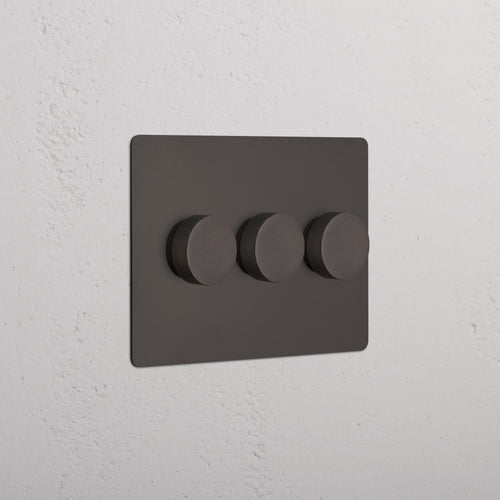 Bronze Kew 3G Dimmer Switch with three round knobs on a textured white wall.