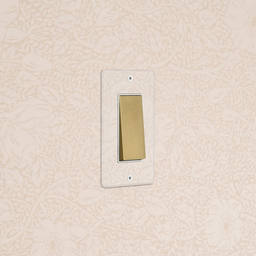 Kew 1G Four Way Rocker Switch in Clear Antique Brass White installed on a patterned wallpapered wall.