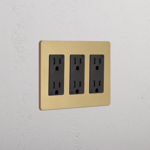 Grove 3G Outlet in Antique Brass Black with three black electrical outlets, mounted on a white wall.