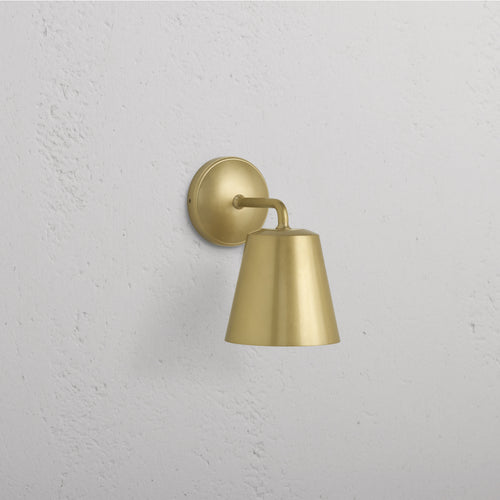 Richmond Medium Wall Light in Antique Brass with round base and conical shade, mounted on a white wall.