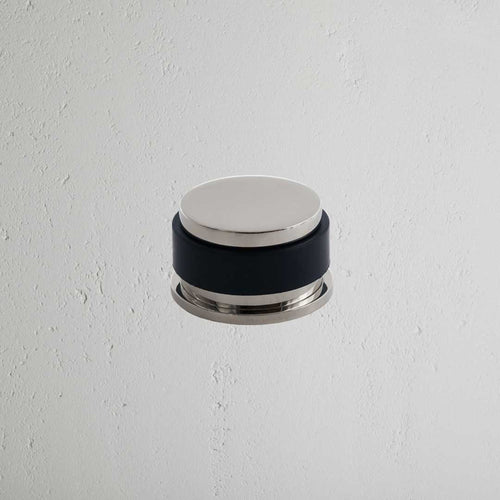 Seymour Door Stop in polished nickel with black rubber center, mounted on a textured white wall.