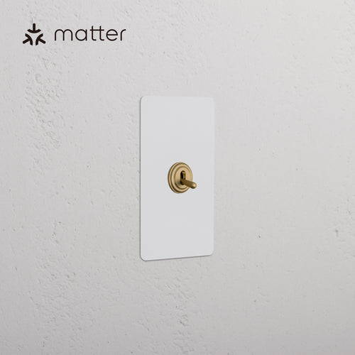 Kew 1G Smart Retractive Toggle Switch in paintable antique brass finish, mounted on a white wall.
