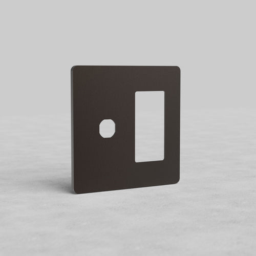 Bronze 2-gang switch and outlet plate (Grove US) with one round and one rectangular cutout, upright on a light surface.