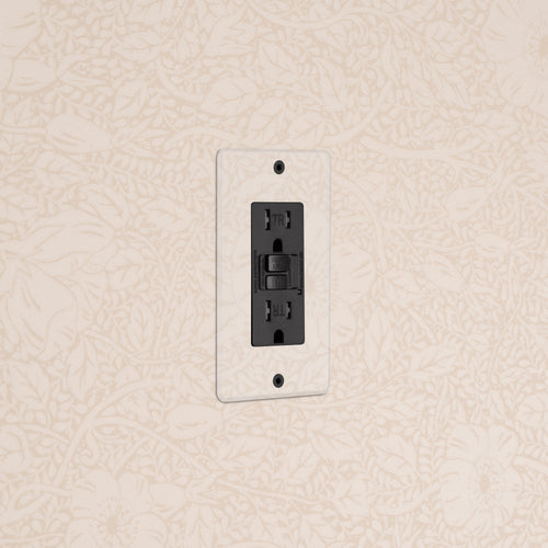 Kew 1G 15A GFCI Outlet in Clear Black with reset and test buttons, mounted on a light floral wall.