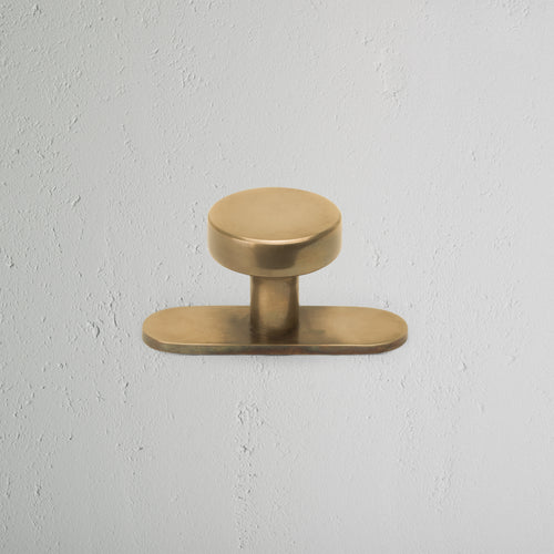 Polished Kilburn Furniture Knob with a round design, mounted on a light textured white wall.