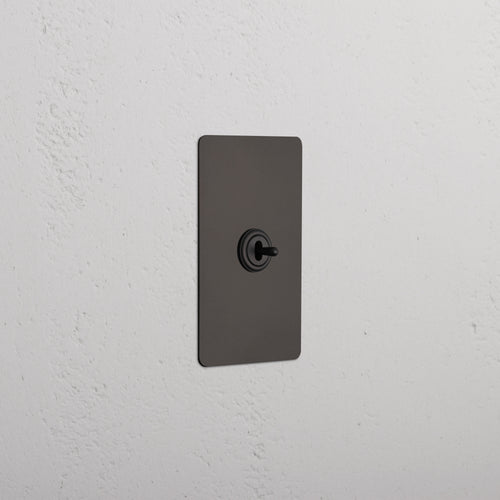 Kew 1G Center Retractive Toggle Switch in bronze finish, featuring a central circular toggle on a standard plate.