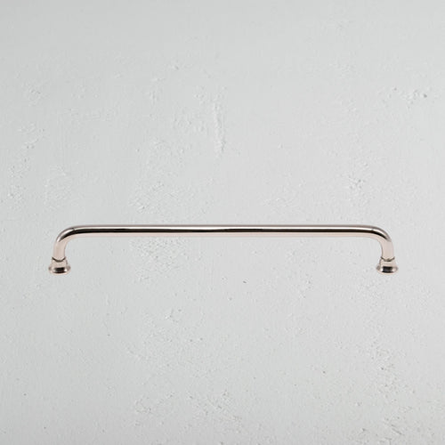 Sycamore Furniture Handle Medium in polished nickel, gently curved and mounted on a white textured surface.