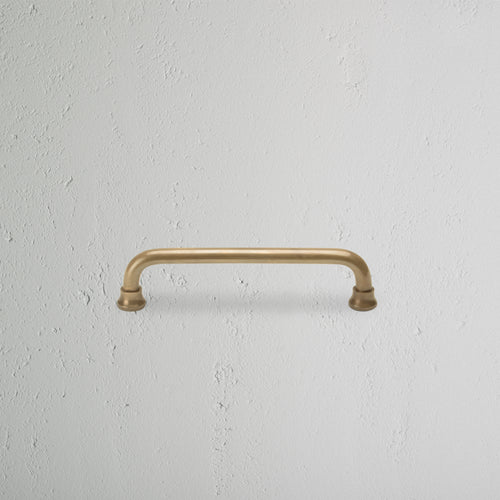 Sycamore Furniture Handle Small in antique brass finish, shown mounted on a white textured surface.