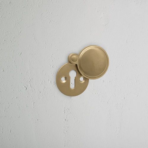 Warwick Covered Key Escutcheon in Antique Brass with round cover, partially open to show keyhole.