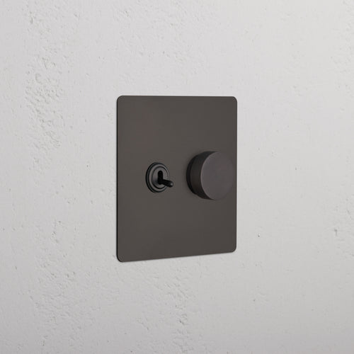 Bronze Kew 2G Toggle & Dimmer Switch with left toggle and right dimmer knob, shown on a white wall.