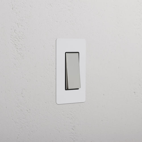 Kew 1G Rocker Switch in paintable polished nickel black finish, installed on a white textured wall.