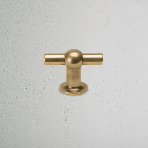 Harper T-Bar Furniture Handle Medium in antique brass, T-shaped, mounted on a light gray textured surface.