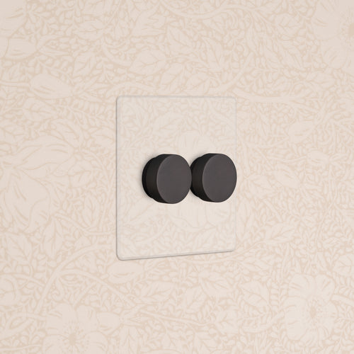 Kew 2G Dimmer Switch in clear bronze finish with two black rotary dials, mounted on a beige wall.