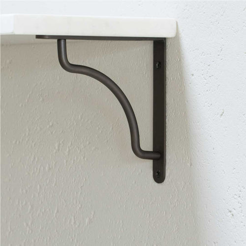Kilburn Shelf Bracket Small in bronze, mounted on a white wall, supporting a white shelf with a curved support bar.