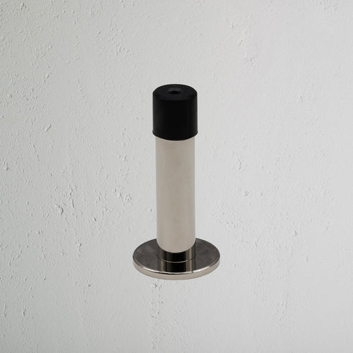 Montpelier Door Stop in polished nickel with black rubber tip, mounted on a white textured wall.