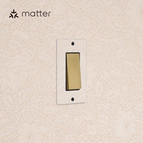 Kew 1G Smart Retractive Rocker Switch in clear antique brass with black trim, mounted on floral-pattern wallpaper.