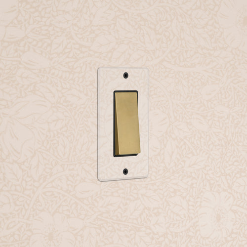 Kew 1G Four Way Rocker Switch in clear antique brass with black rockers, mounted on a wall.
