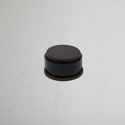 Bronze Seymour Door Stop with a rounded design mounted on a light textured white wall.