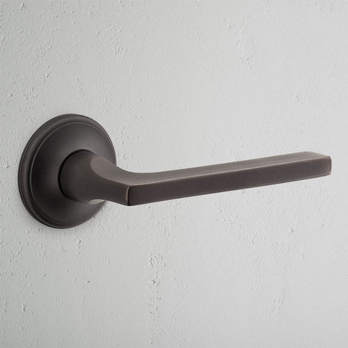 Clayton Passage Door Handle Set in bronze with a modern, rectangular design mounted on a light gray wall.