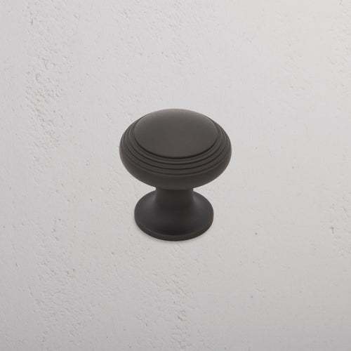 Medium-sized round bronze Barlow furniture knob with ridged detailing, shown on a textured white surface.